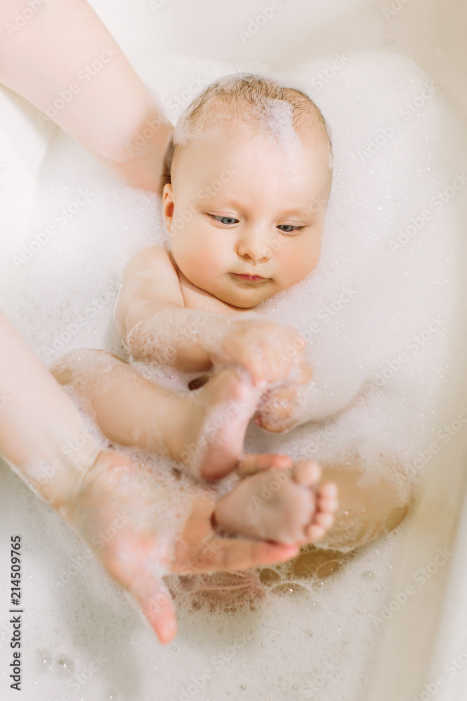 Happy laughing baby taking a bath playing with foam bubbles. Little