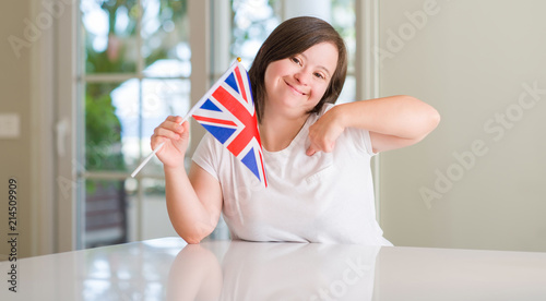 Down syndrome woman at home holding flag of uk with surprise face pointing finger to himself