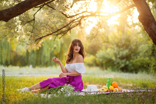 Beautiful girl with a peach in her hands on a picnic in the park. Looking away