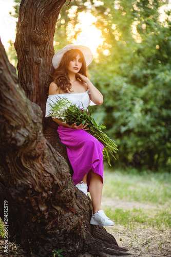 next to the tree standing a beautiful lady with a bouquet of wildflowers. Lifestyle in the countryside