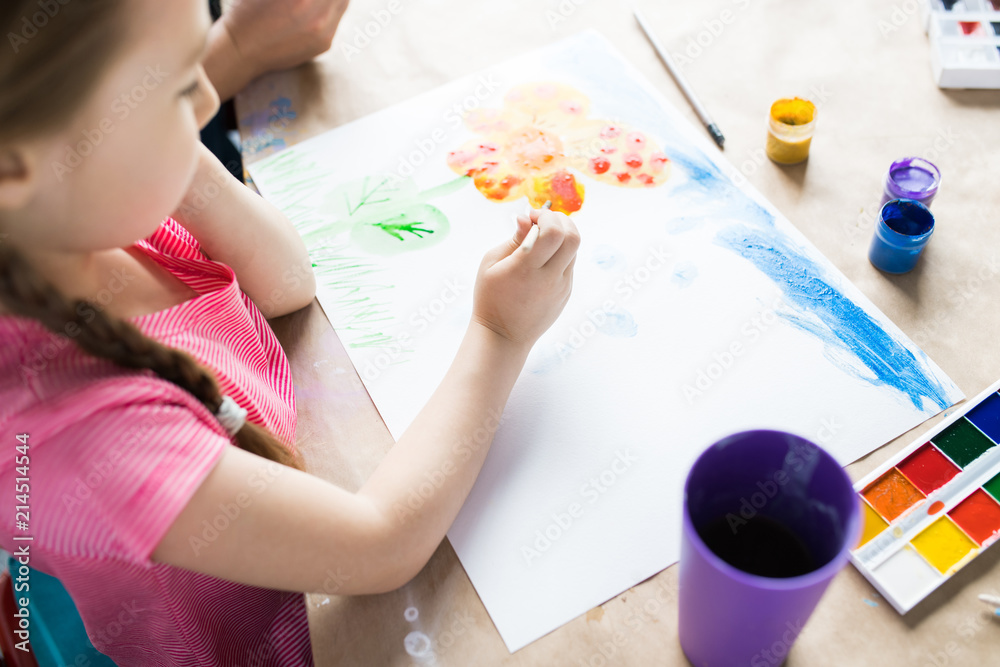 Little girl sitting at the table painting and using watercolor paints Little girl sitting at the table painting and using watercolor paints