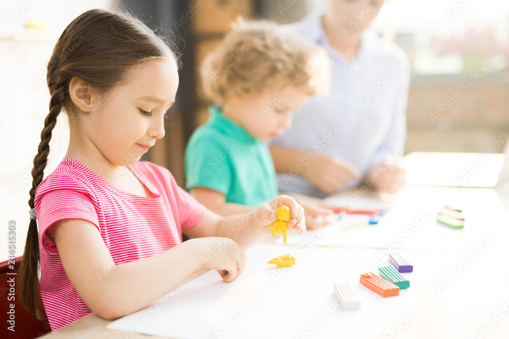Little girl sitting at the table and play dough and mold from plasticine in art school Little girl sitting at the table and play dough and mold from plasticine in art school