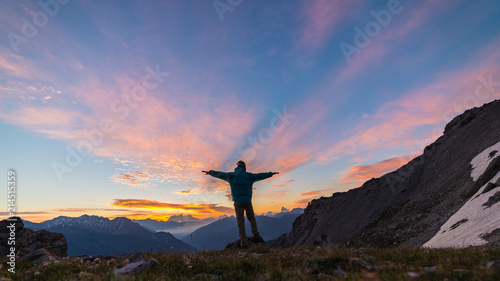 Photos Man standing on mountain top outstretching arms, sunrise light colorful sky scenis landscape, conquering success leader concept