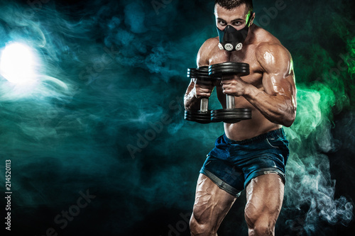 Muscular young fitness sports man in training mask. Workout with dumbbell in fitness gym. Copy space for fitness nutrition ads.