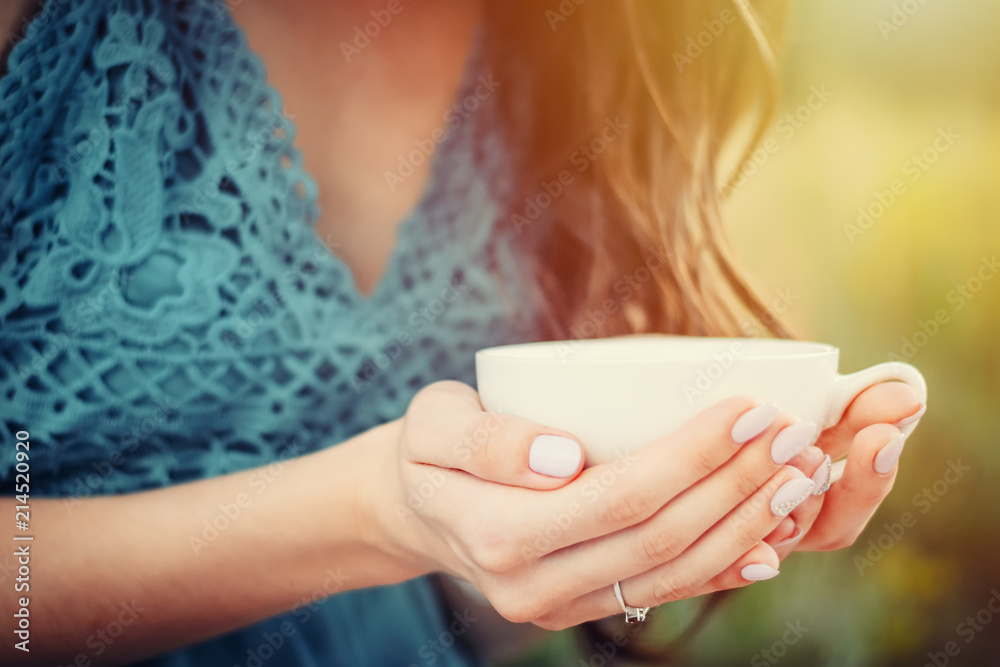 young woman or girl holds white cup in hands. Toned photo with summer sunlights young woman or girl holds white cup in hands. Toned photo with summer sunlights