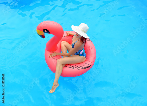 A young woman wearing a bathing suit and  a white summer hat sits relaxed in an  inflatable swim ring. 