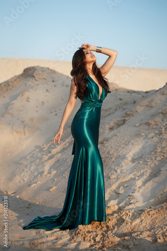 Fashion portrait of a sexy girl in a chic long green dress in a sandy desert.