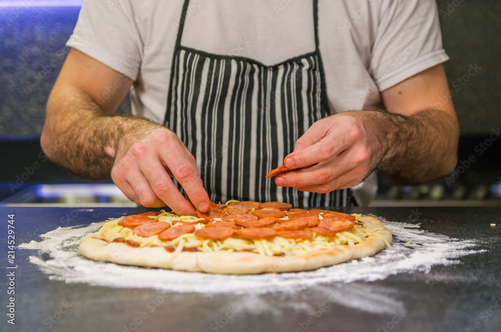 Man preparing pepperoni pizza on black granite table