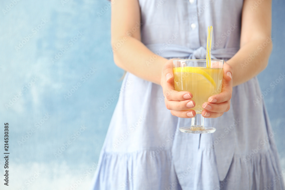 Young woman holding glass with lemon cocktail against color background Young woman holding glass with lemon cocktail against color background