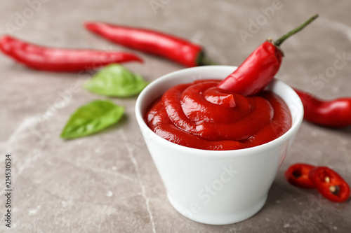 Foto Bowl with spicy chili sauce and fresh pepper on gray table