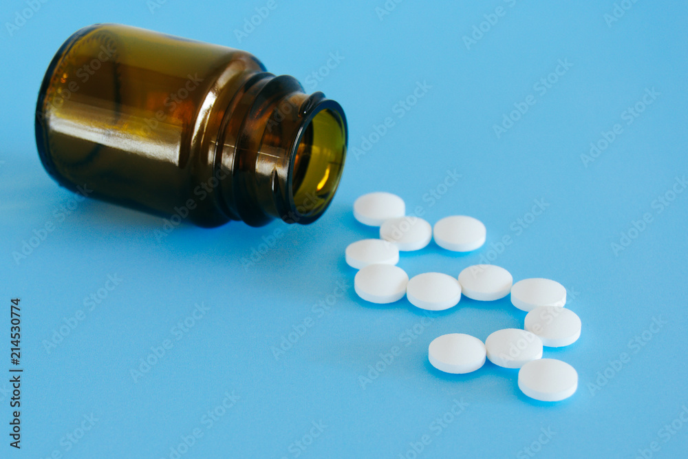 White pills spilling from a medicine bottle forming a dollar sign on a blue background. White pills spilling from a medicine bottle forming a dollar sign on a blue background.