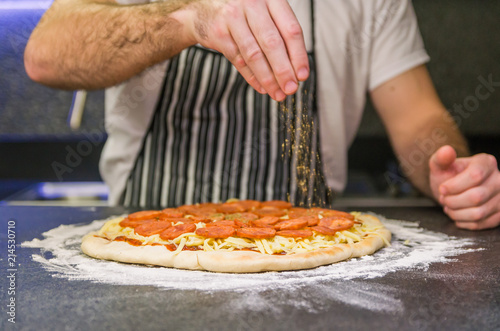 Man preparing pepperoni pizza on black granite table