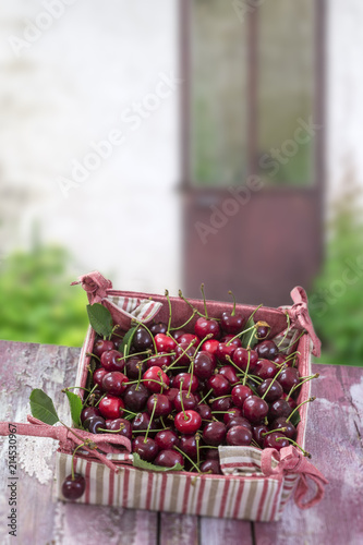 rzd fresh cherry with leaves on cardboard box in red and white fabric,on old garden housse doord background. view, copy space photo