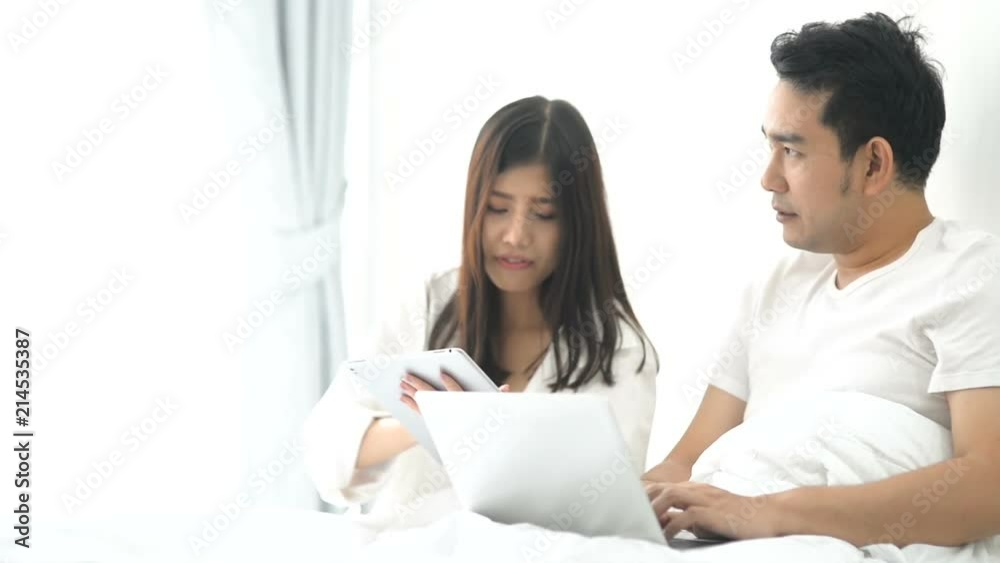 Happy Asian couple using tablet and laptop on bed and talking together. Happy Asian couple using tablet and laptop on bed and talking together.