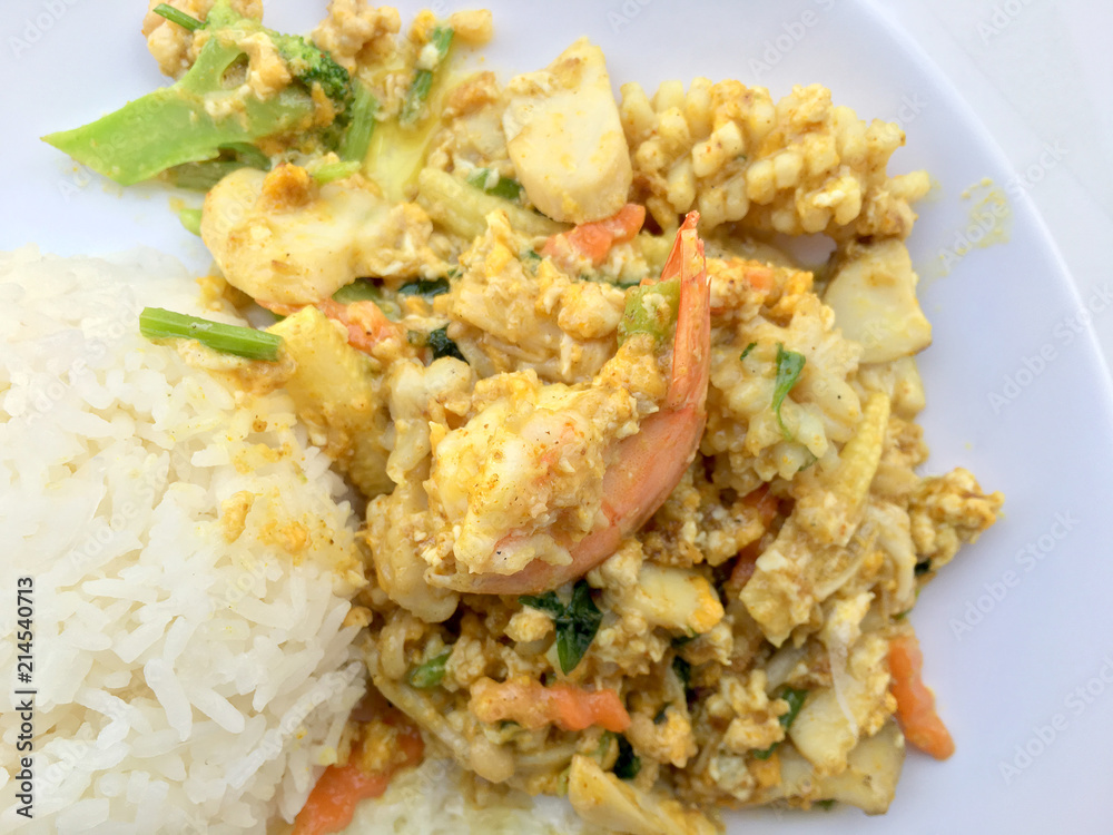 Stir-fried seafood, prawn and squid with yellow curry powder with rice and fried egg in white plate on white background. Thai style food. Stir-fried seafood, prawn and squid with yellow curry powder with rice and fried egg in white plate on white background. Thai style food.