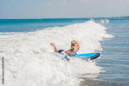 Happy baby boy - young surfer ride on surfboard with fun on sea waves. Active family lifestyle, kids outdoor water sport lessons and swimming activity in surf camp. Summer vacation with child photo
