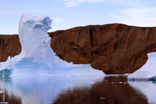 An amazing iceberg set against the backdrop of a brown glacial mountain.