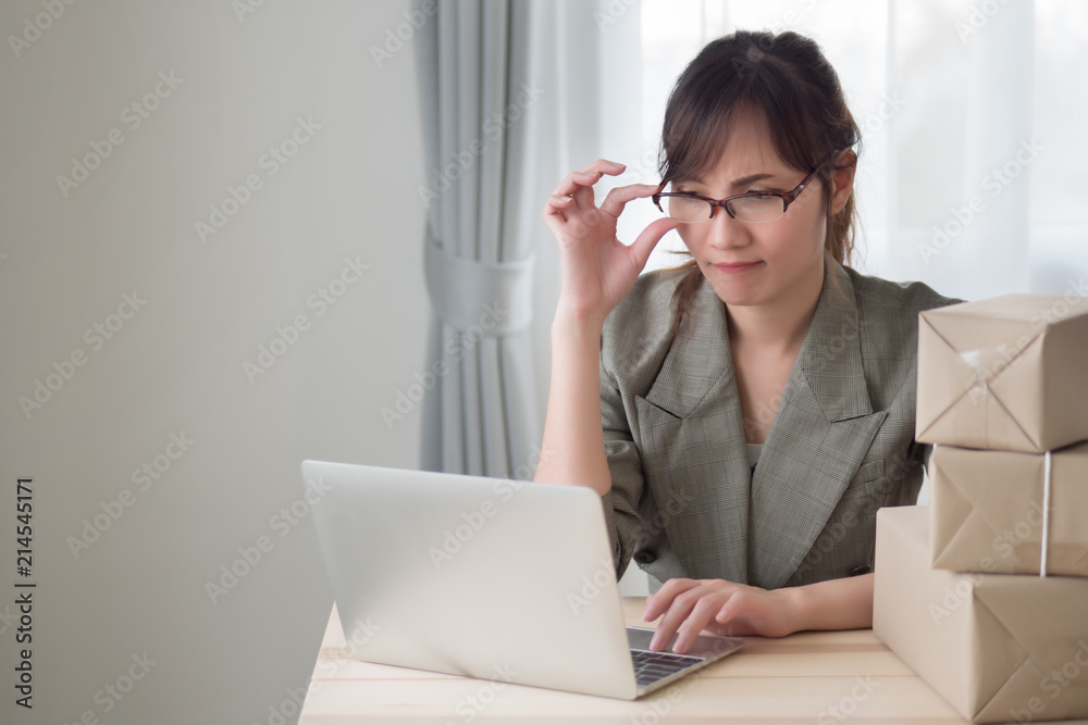 stressed asian woman working with her laptop computer and courier parcel box; portrait of sad stress unhappy woman business owner with business failure, loss concept; adult asian chinese woman model stressed asian woman working with her laptop computer and courier parcel box; portrait of sad stress unhappy woman business owner with business failure, loss concept; adult asian chinese woman model