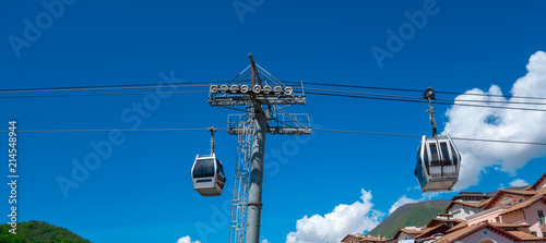 Two cabins on a cable car under the clear blue sky, near mountains peaks and hauses roofs. Bottom view, mountainsite of Sochi, Caucasus photo