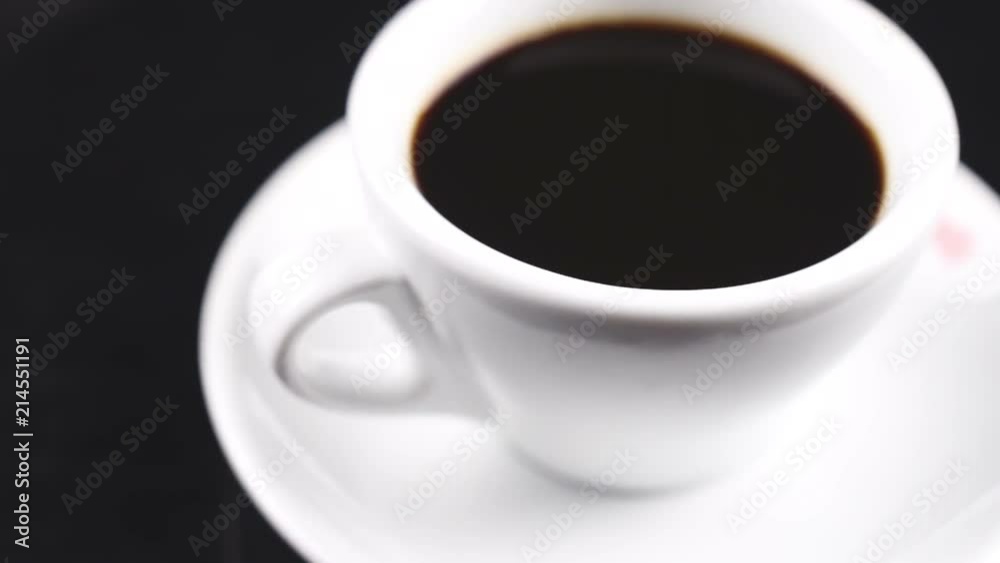 Black coffee in white cup on plate rotating on dark surface. Black coffee in white cup on plate rotating on dark surface.