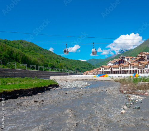 Two cabins on a cable car above a river. Under the clear blue sky, near mountains peaks and hauses roofs. Bottom view, mountainsite of Sochi, Caucasus photo