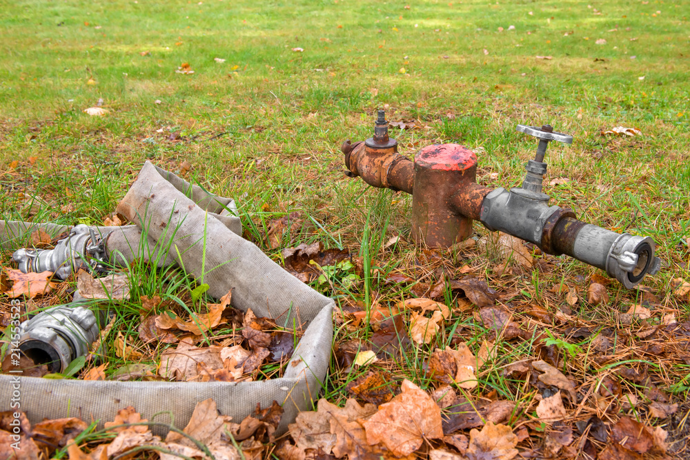 Fire hydrant with a hose in an autumn park covered with yellow leaves Fire hydrant with a hose in an autumn park covered with yellow leaves