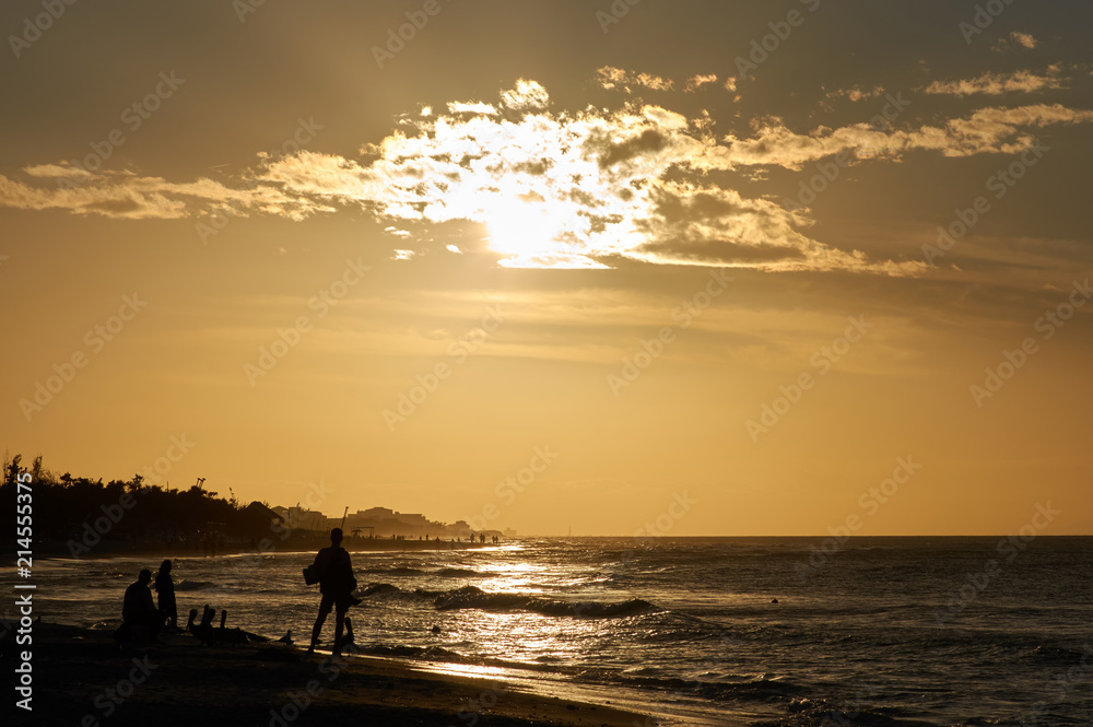 Evening beach at sunset with dark figures of fishermen