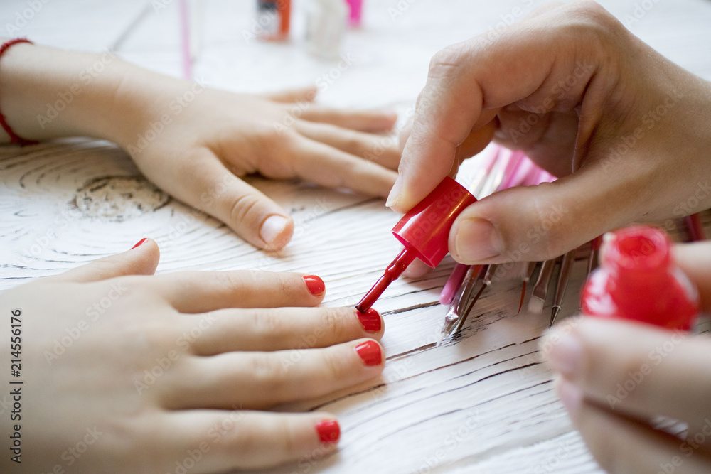 custom made wallpaper toronto digitalmom paints daughter's nails on hands with red nail Polish on white table, beautiful nails concept, manicure
