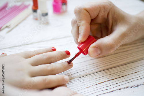 mom paints daughter s nails on hands with red nail Polish on white table  beautiful nails concept  manicure