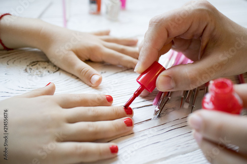 mom paints daughter's nails on hands with red nail Polish on white table, beautiful nails concept, manicure