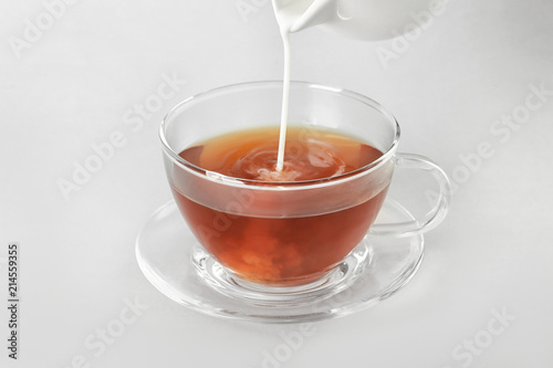 Adding milk to delicious tea on light background