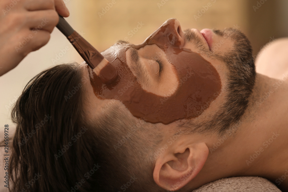 Naklejka premium Beautician applying cosmetic mask on man's face in spa salon