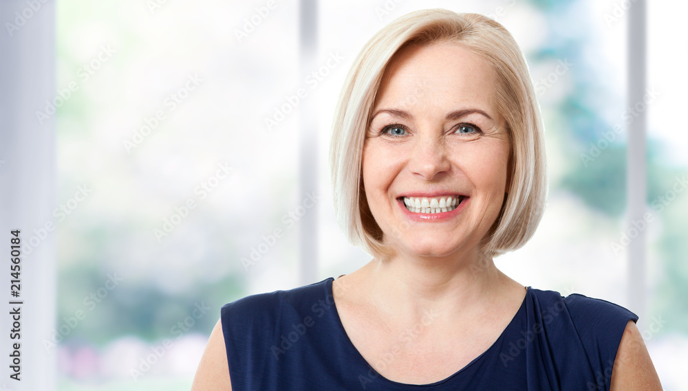 Obraz premium Atrakcyjna kobieta w średnim wieku z pięknym uśmiechem przy oknie.