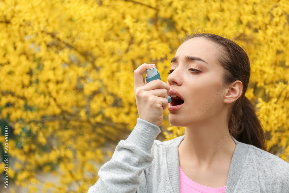 Young woman using inhaler near blooming tree. Allergy concept Young woman using inhaler near blooming tree. Allergy concept