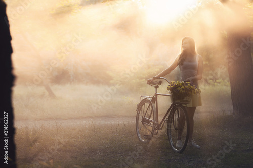  Beautiful young girl in dress walking in the park on a bicycle. Sports lady and fog.