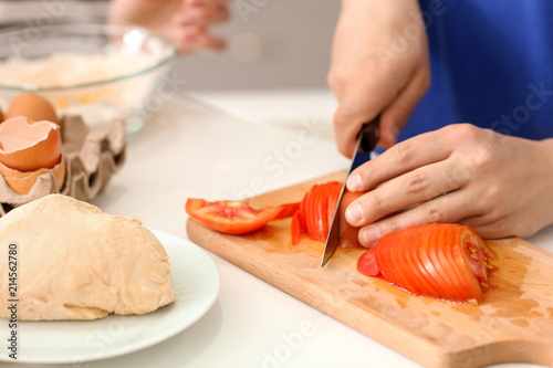 Young man cutting tomato on wooden board in kitchen