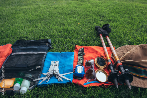 Set of equipment for hiking and travel on green grass with copy space . Items include trekking pole, multi tool, flashlight, hygiene products, tracking clothes, sleeping bag, first aid kit