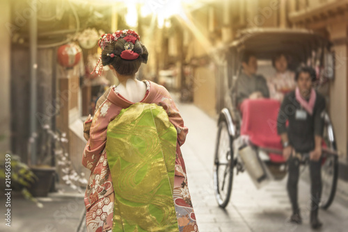 Maiko walking in an alley of Kyoto in the sunset light crossing a rickshaw.