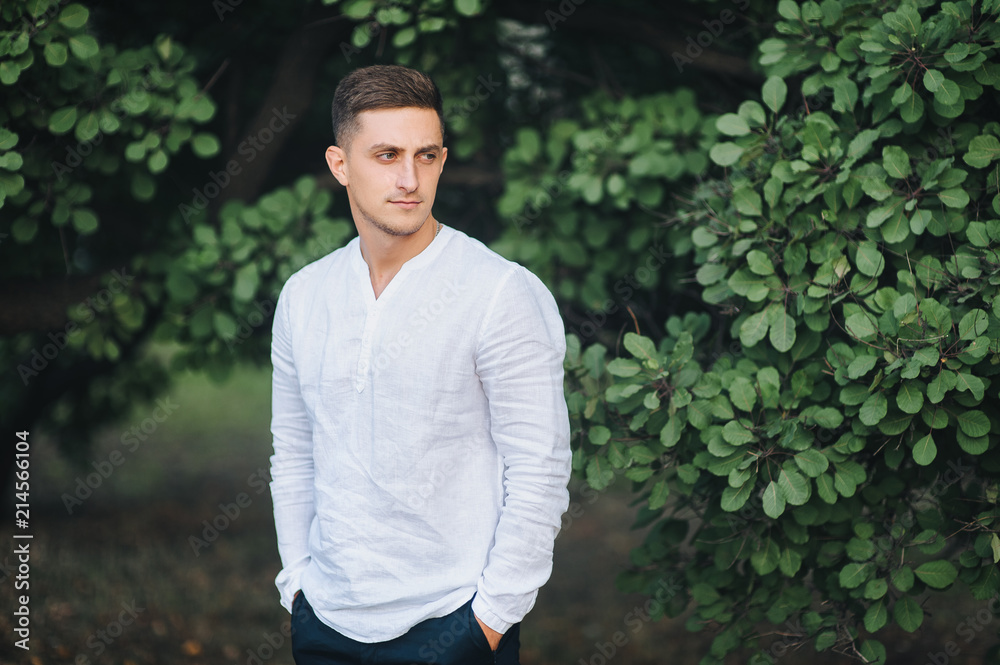 Stylish and young groom stands on a background of green foliage and trees. Wedding portrait of a beautiful groom. Stylish and young groom stands on a background of green foliage and trees. Wedding portrait of a beautiful groom.