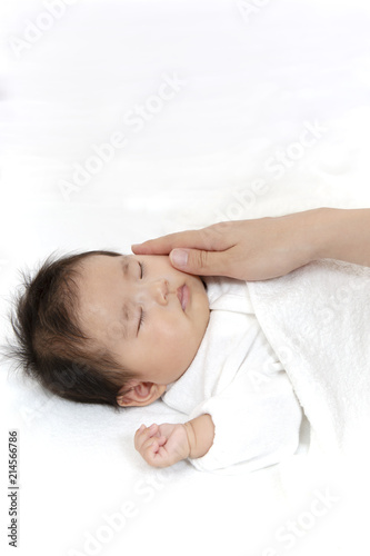 寝ている新生児に手を添え撫でる母の手