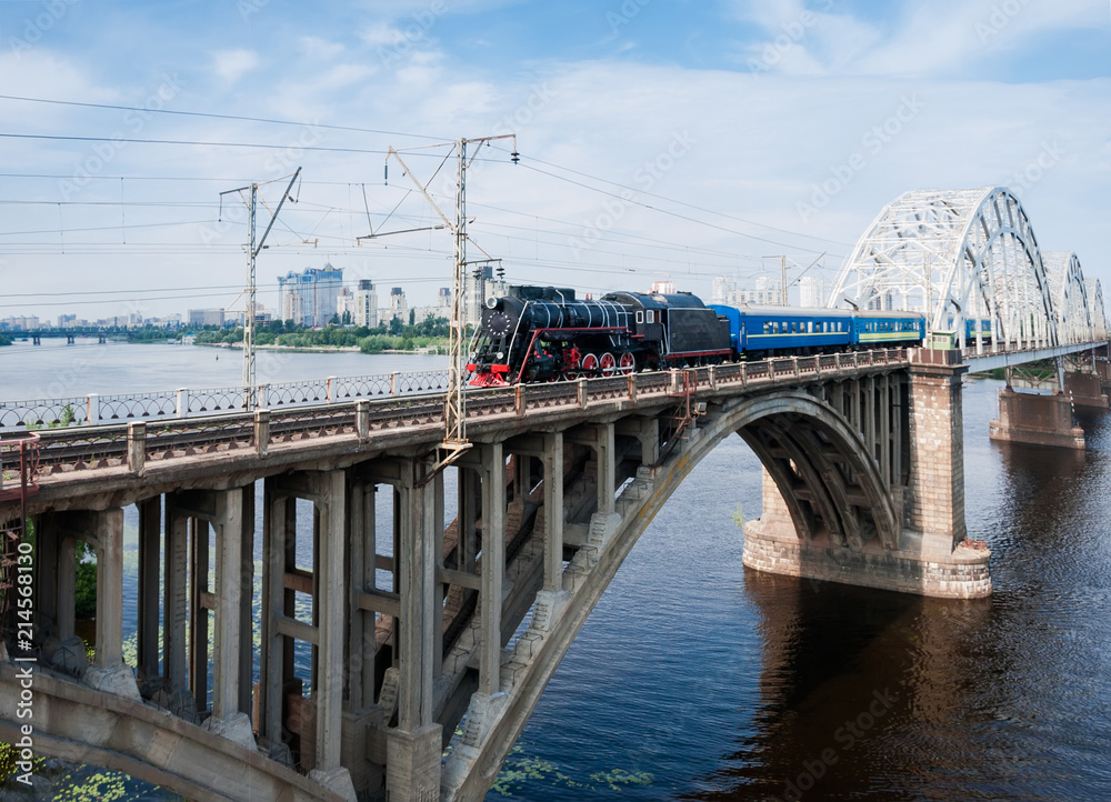 Steam locomotive with passenger train in motion on bridge