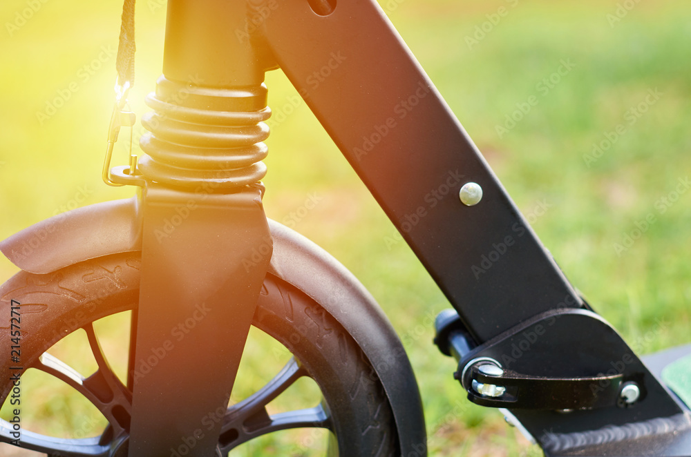 Black folding kick scooter, close up parts, front wheel, sunlight effect