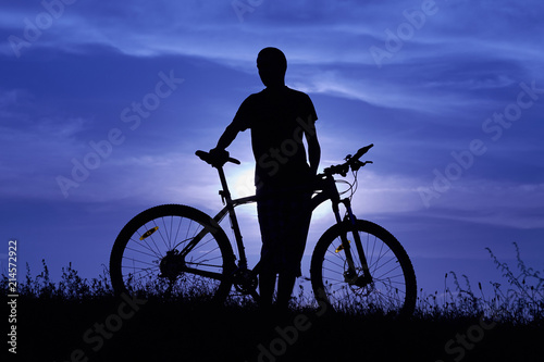 Silhouette of a young man with a bicycle at sunset.