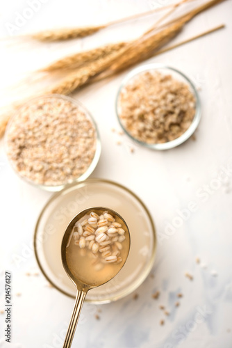 Barley water in glass bowl with spoon and raw and cooked pearl barley wheat seeds. selective focus
