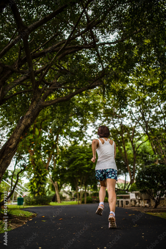 Asian woman jogging in the park, shooting from behind with big trees background Asian woman jogging in the park, shooting from behind with big trees background