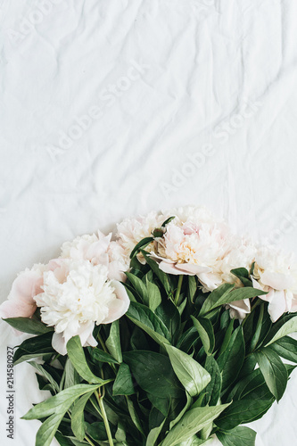 Flat lay, top view of white peonies flower bouquet on white blanket background.