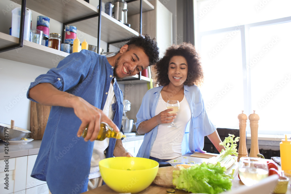 Young African-American woman drinking wine and her boyfriend cooking in kitchen