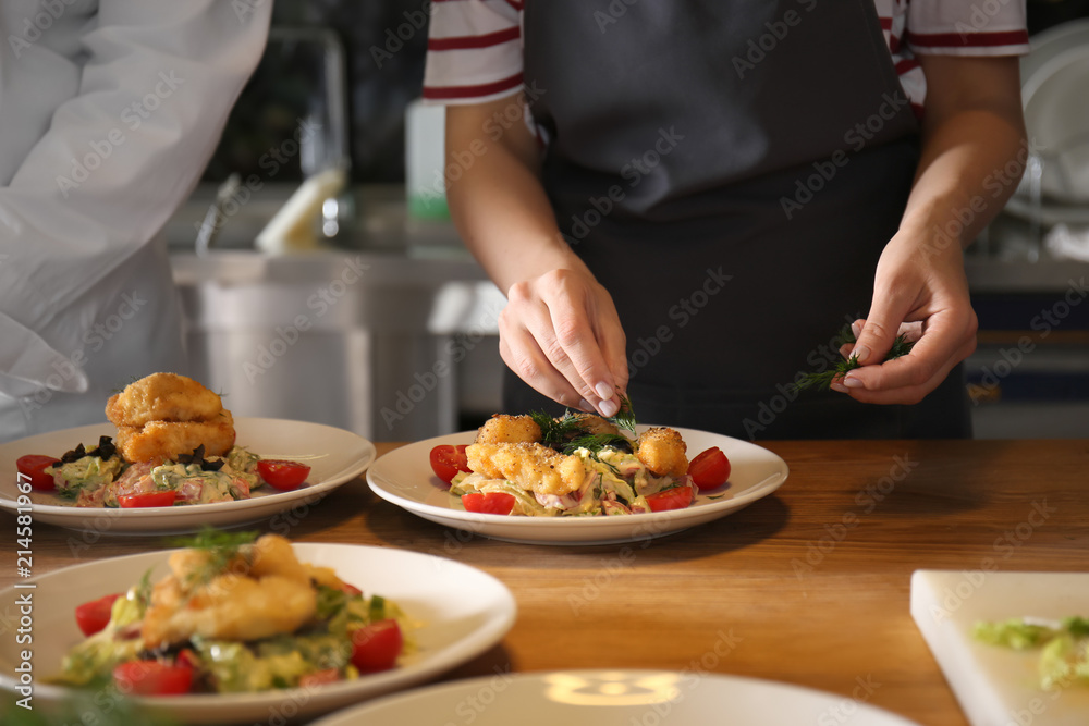 Young woman preparing tasty meat and salad during cooking classes in restaurant kitchen