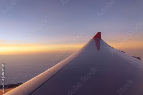 Airplane wing flying above clouds sunrise