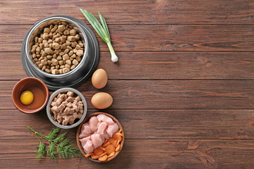 Bowls with pet food and natural products on wooden background